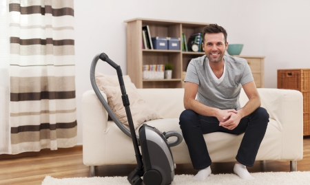 Portrait of smiling man with vacuum cleaner in living room の写真素材