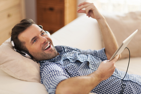 Happy man listening music and lying down on sofa 
の写真素材