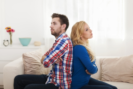 Angry young couple sitting back to back at home の写真素材