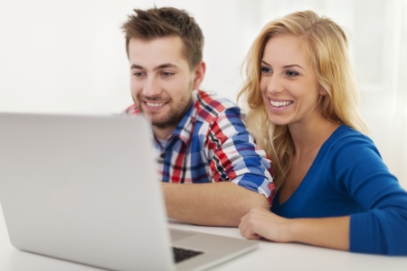 Smiling couple looking on laptop at homeの写真素材