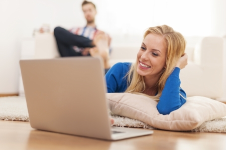 Smiling woman lying down in living room with laptop の写真素材