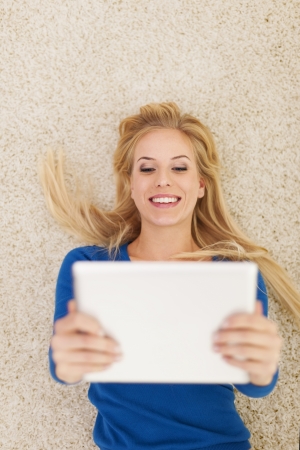 Smiling beautiful woman lying on carpet and using digital tablet の写真素材