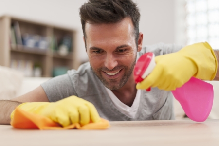 Smiling man cleaning desk in living room の写真素材