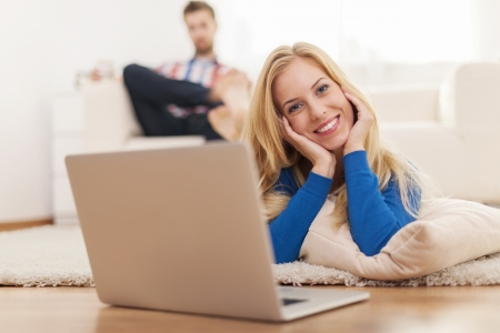 Cute blonde woman relaxing with laptop on carpet at home の写真素材