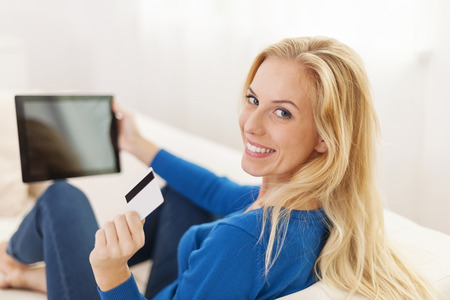 Blonde woman holding digital tablet and showing credit card の写真素材