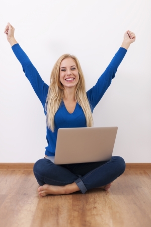 Excited woman with laptop sitting on floor の写真素材
