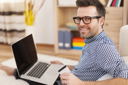 Happy man with laptop and credit card at home の写真素材