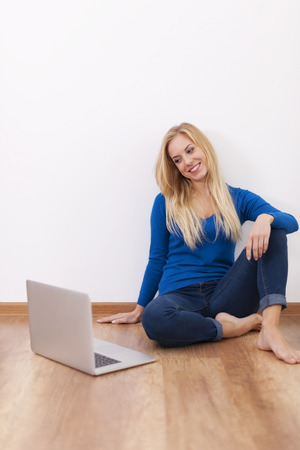 Blonde young woman sitting on hardwood floor with laptop の写真素材