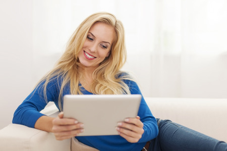 Beautiful blonde woman using digital tablet on sofaの写真素材