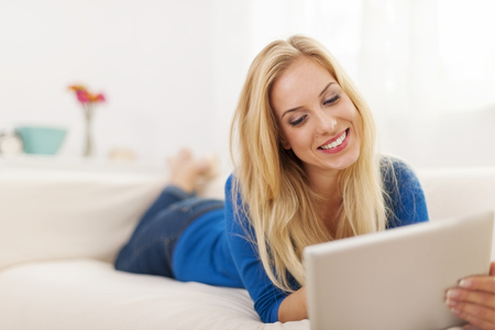 Beautiful woman lying down on couch and using digital tablet の写真素材