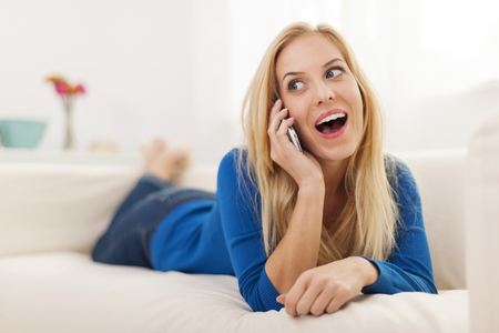 Shocked woman lying down on sofa and talking on the phone 
の写真素材