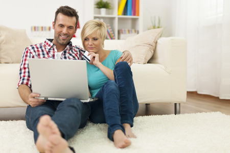 Couple sitting on carpet at home and doing shopping onlineの写真素材