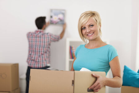 Smiling blonde woman holding carton box during the moving home の写真素材