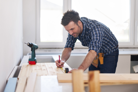 Smiling carpenter measuring wooden planksの写真素材