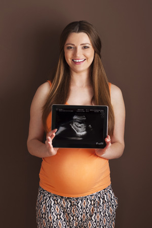Beautiful pregnant woman showing ultrasound scan on digital tablet