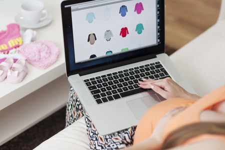 Pregnant woman buying clothes for baby at home using online websiteの写真素材