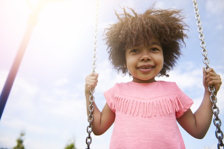 Cute little girl swinging in sunny dayの写真素材