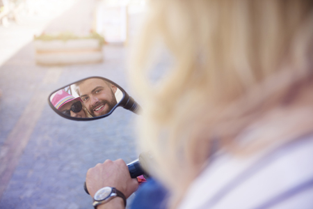 Happy couple reflecting in scooter's mirrorの写真素材