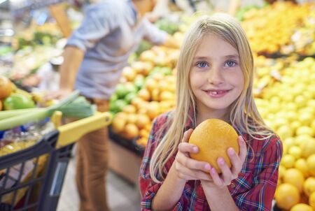 Girl holding orange in grocery store の写真素材