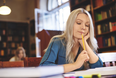 Woman taking notes and reading  in libraryの写真素材