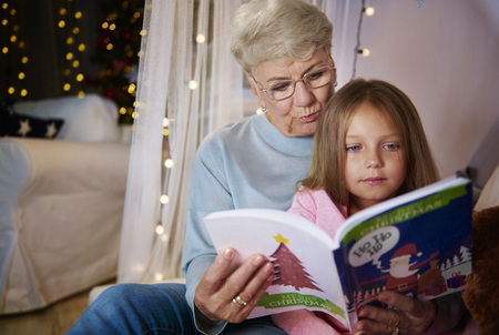 Grandmother and granddaughter reading storybook in bedの写真素材