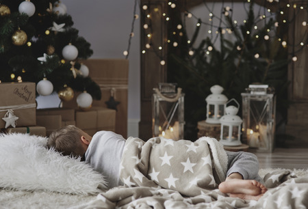 Boy taking a nap next to christmas treeの写真素材