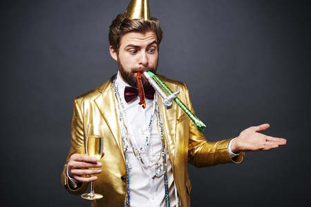 Astonished man with party blower standing with champagne fluteの写真素材