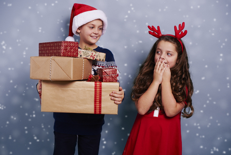 Happy siblings with stack of gifts among snow falling の写真素材