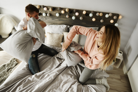 Couple fighting with pillows in bedroom の写真素材