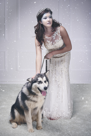 Pretty ice queen with dog among snow falling  の写真素材
