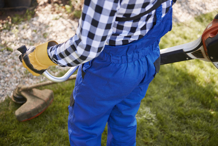 Unrecognizable gardener with weedwacker cutting the grass in the garden