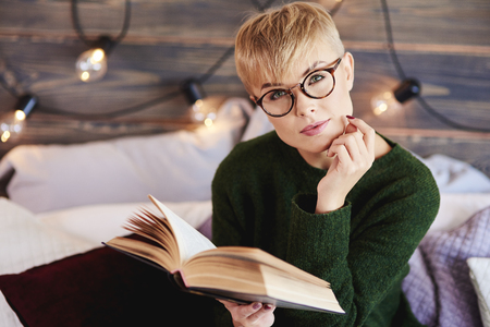 Portrait of beautiful girl reading a book in bedの写真素材