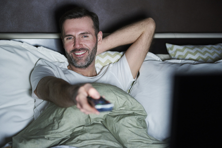 Man lying on the bed and watching tv at nightの写真素材