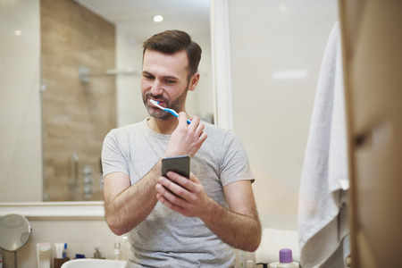 Man brushing his teeth and using mobile phoneの写真素材