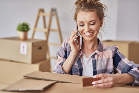 Smiling woman using phone while moving houseの写真素材