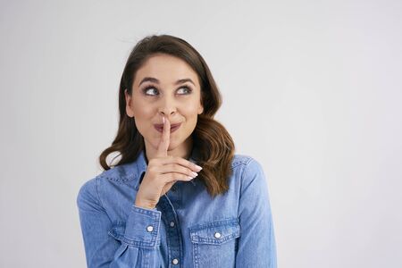 Woman with finger on lips looking up in studio shot