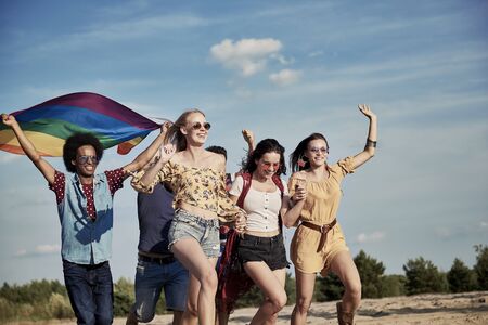 Happy friends with rainbow flag running outdoorsの写真素材