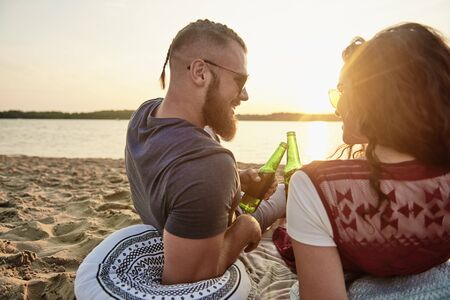 Rear view of young couple drinking beer on the beachの写真素材