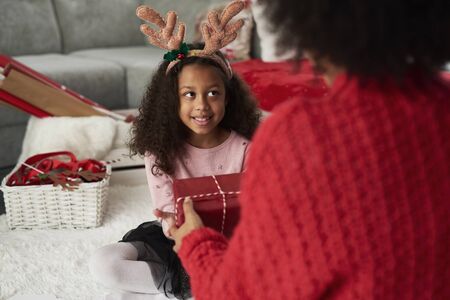Rear view of mommy giving her daughter the Christmas presentの写真素材