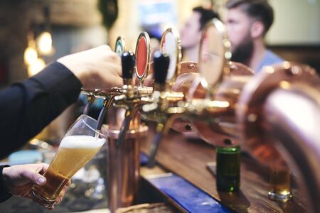 Bartender's hand pouring customer a mug of cold beerの写真素材