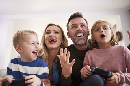 Emotional parents and children playing video game at home