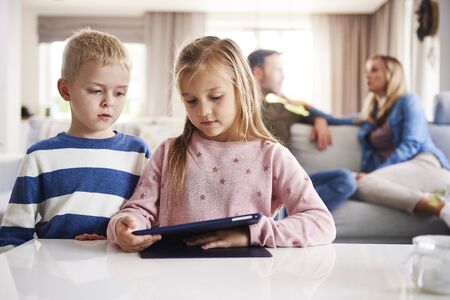 Focused children using technology and parents in the background