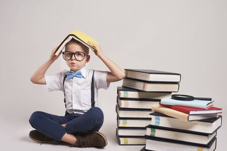 Bored child with stack of books in studio shot の写真素材