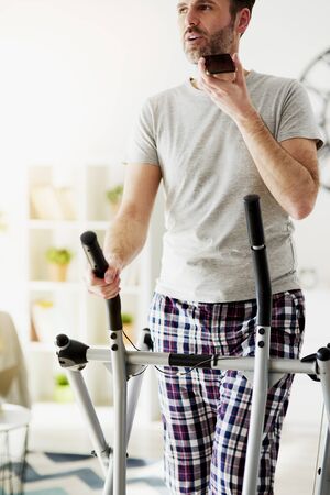 Vertical image of man calling and using a cross trainer