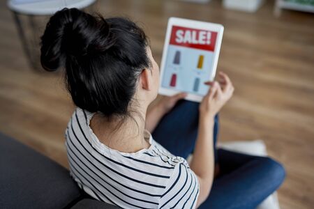 Rear view of young woman watching sales on the tablet.の写真素材