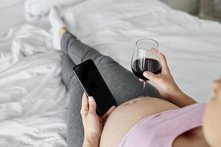 Woman pregnant drinking alcohol in bedの写真素材