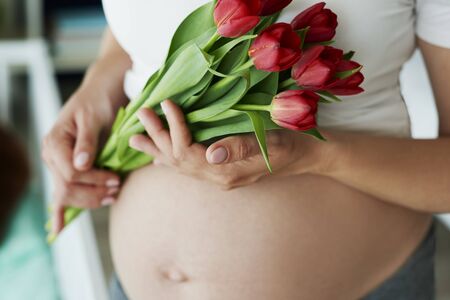 Close up of human pregnant abdomen and bunch of flowersの写真素材