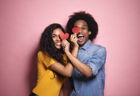 African couple covering eyes by hearts in studio shot.の写真素材
