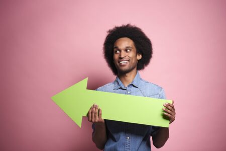 Young African man holding green arrow in a studio shot.