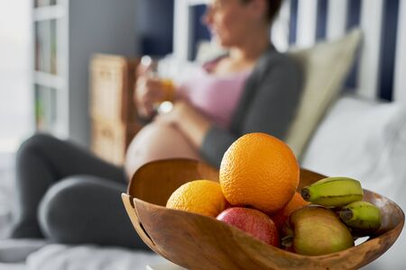 Pregnant woman and bowl of fruits in the foregroundの写真素材